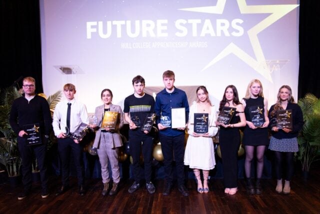 Eight young adults stand on stage holding awards with expressions of pride. The backdrop reads "Future Stars Hull College Apprenticeship Awards."