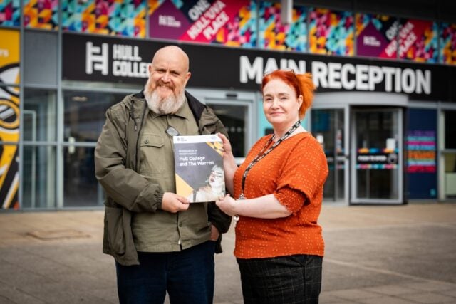 A man and woman stand outside Hull College's vibrant main entrance, holding a brochure titled "Hull College and The Warren," smiling warmly.