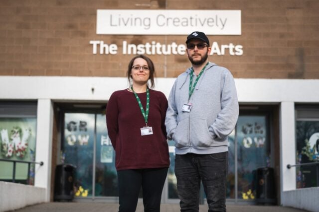 Two people stand confidently outside a building labelled "The Institute of Arts," conveying a sense of creativity and professionalism.