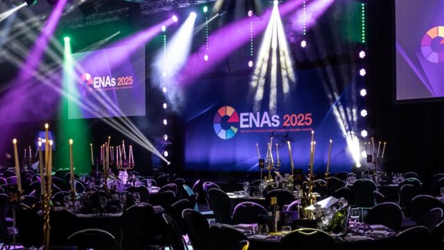 A dimly lit event venue with tables and candelabras, spotlighted stage showing "ENAs 2025" logo. Atmosphere is elegant and festive.