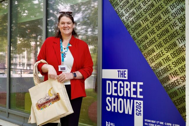 A smiling person in a red jacket holds a beige tote bag, standing beside a blue "The Degree Show 2025" poster. Bright, academic, and welcoming scene.
