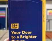 A hand holds a blue and yellow "14+ College" prospectus titled "Your Door to a Brighter Future." The background shows a matching college sign.