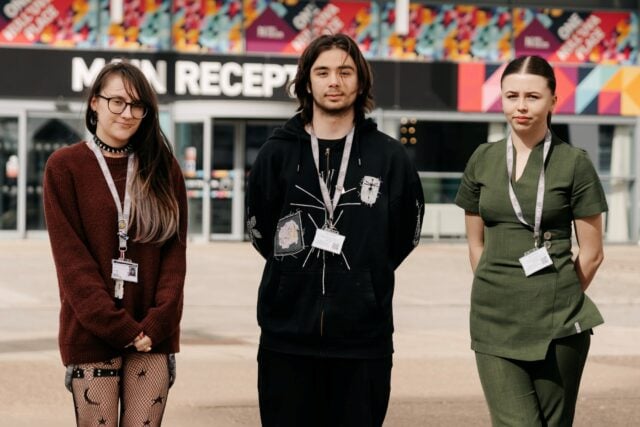 Three students standing in front of a colourful building labelled "Main Reception."