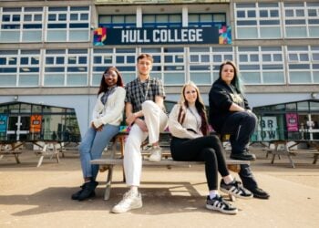 Four students sit and lean on a wooden bench outside Hull College. They appear relaxed and confident, with the college's modern building in the background.