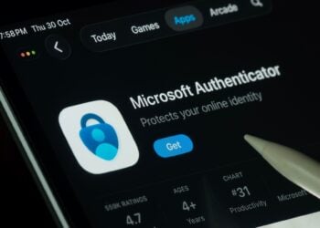 Close-up of a tablet showing the Microsoft Authenticator App Store page, with its blue lock icon, rating details, and a stylus pointing toward it.