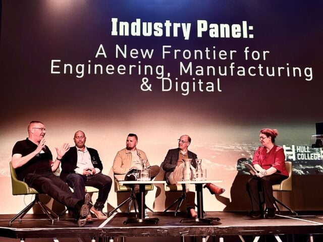 ive panelists sit onstage beneath the title “Industry Panel: A New Frontier for Engineering, Manufacturing & Digital,” in a formal, discussion-focused setting.